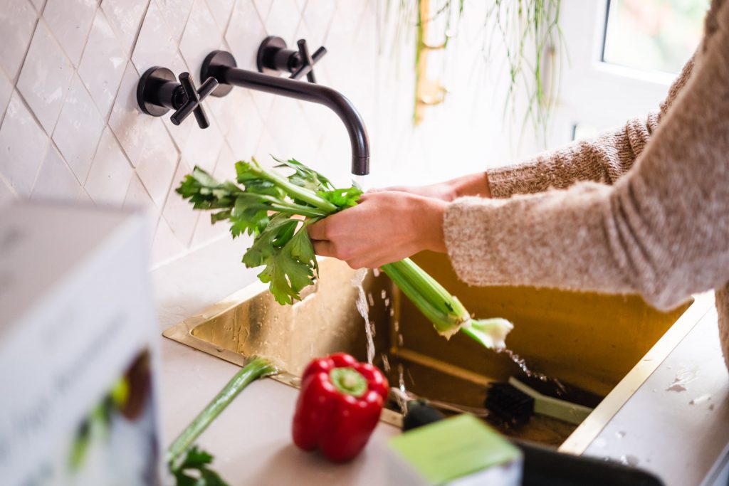 Frau wascht Sellerie in modernen Wasserhahn