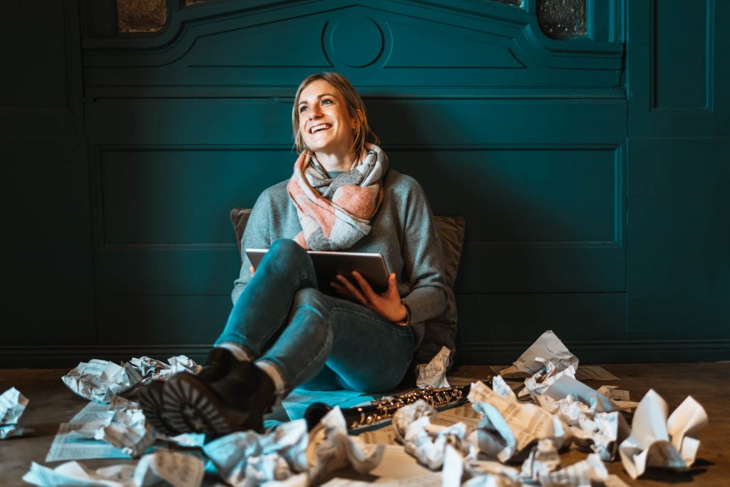 Frau lacht sitzt mit Noten und Klarinette auf Boden mit ipad