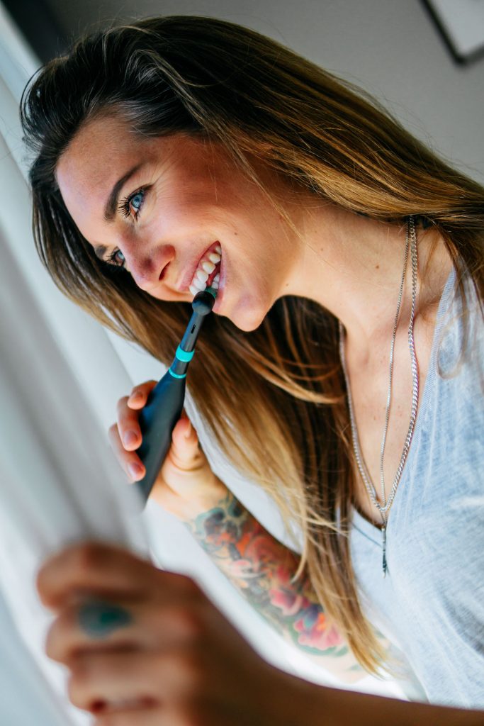 Lifestyle Fotoshooting Happybrush Frau steht mit elektrischer Zahnbürste vor Fenster