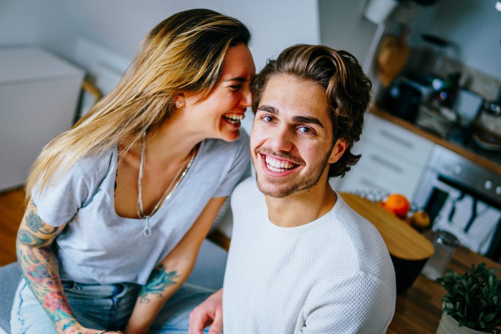 Paar sitzt in Wohnung und lacht bei Fotoshooting Lifestyle Happybrush