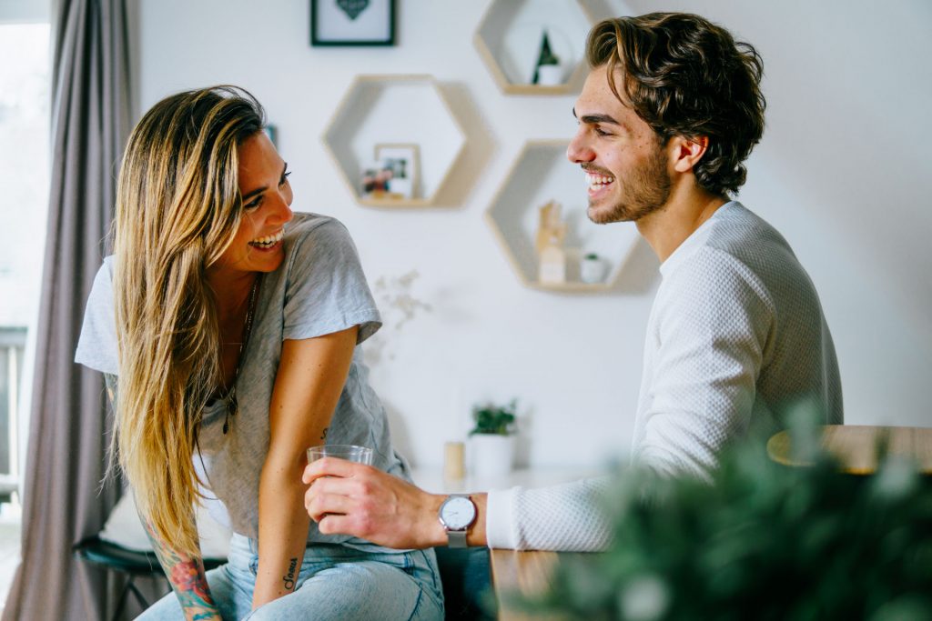 Paar sitzt in Wohnung und lacht bei Fotoshooting Lifestyle Happybrush