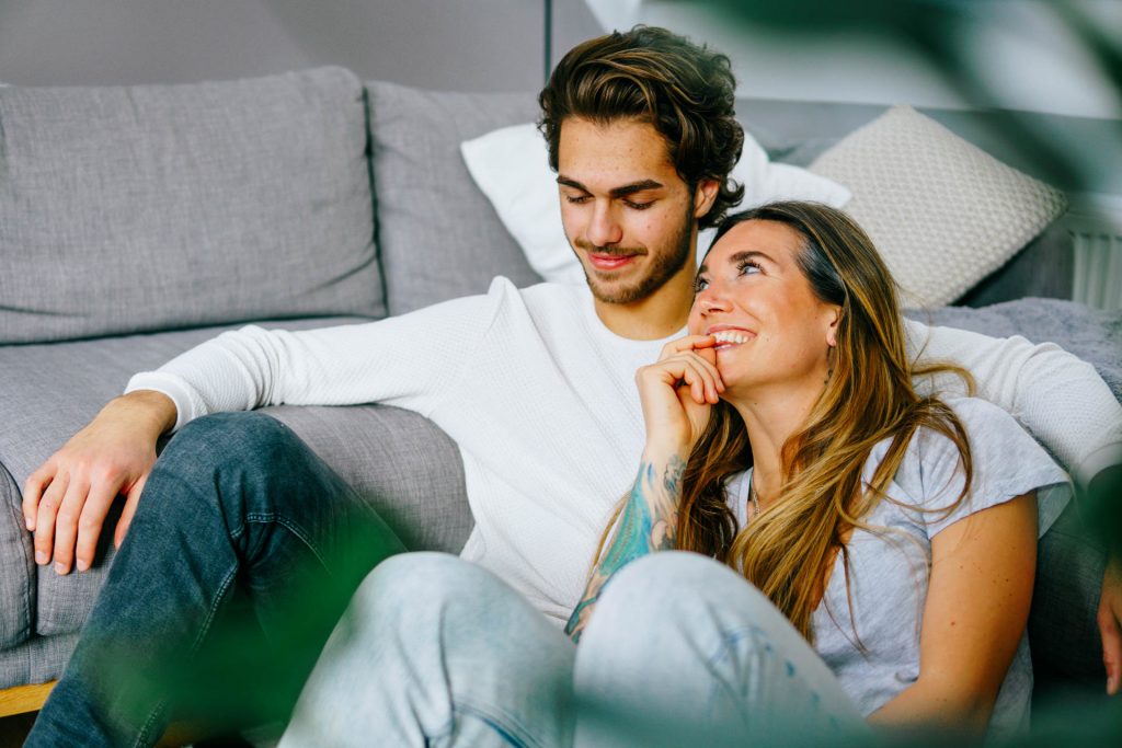 Paar sitzt in Wohnung und lacht bei Fotoshooting Lifestyle Happybrush