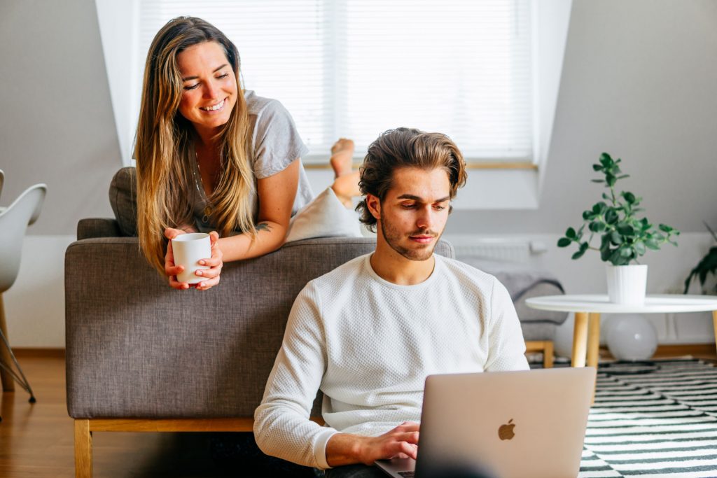 Paar sitzt in Wohnung und lacht bei Fotoshooting Lifestyle Happybrush Remote Work Arbeit Laptop